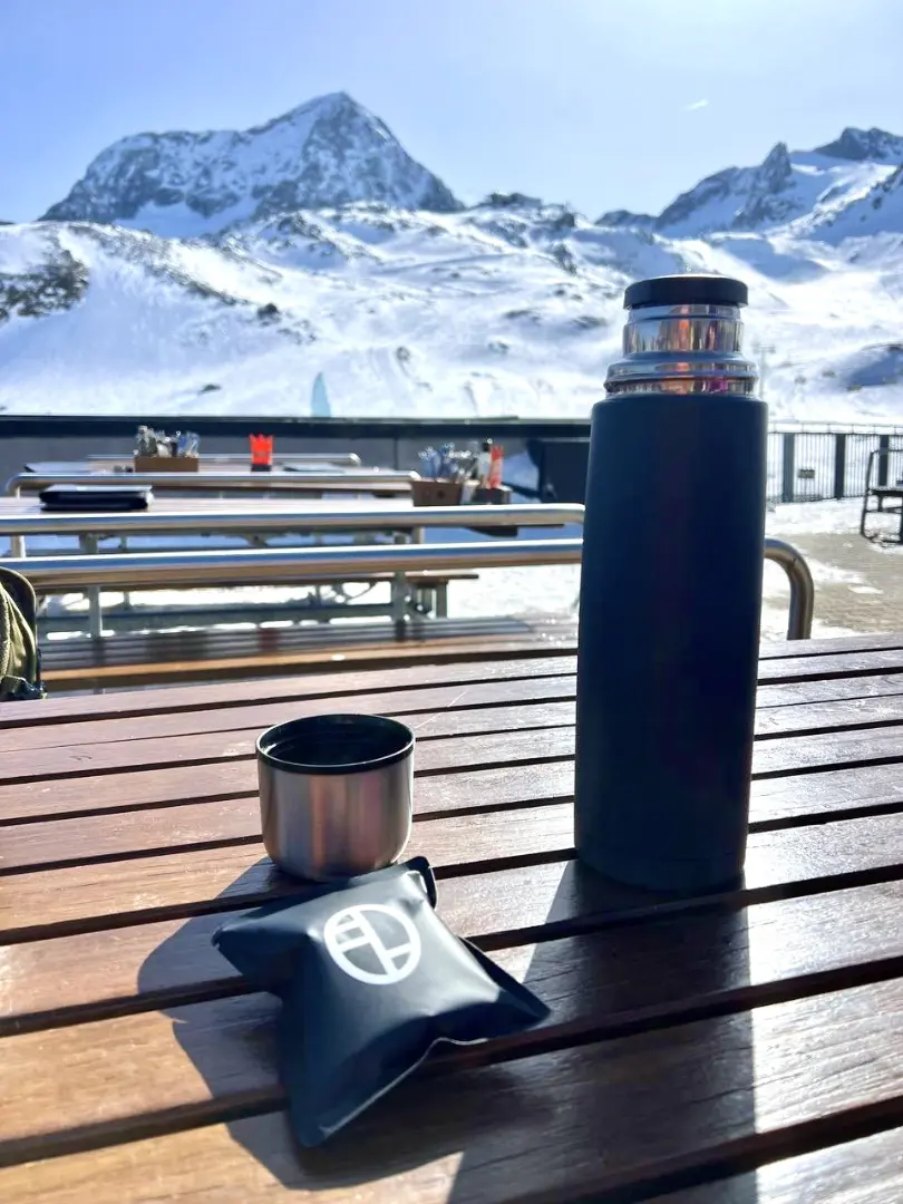 Skier taking a drip coffee bag to a ski resort woth a thermos to enjoy specialty coffee outdoors.